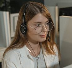 A young woman with eyeglasses and headphones working in a call center.